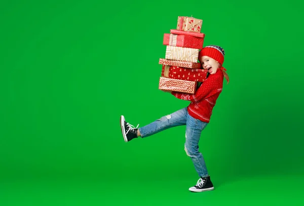 Happy funny child girl in red Christmas hat   with gifts on gree — Stock Photo, Image