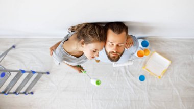 Genç ve yorgun çift evlerinde duvar boyuyor.