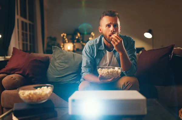 Joven hombre viendo proyector tv en casa por la noche alon — Foto de Stock