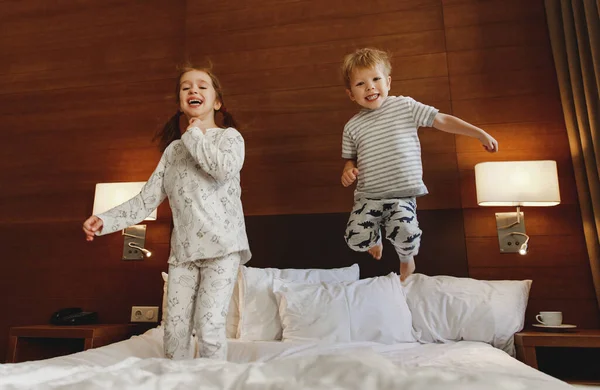 Happy children brother and sister jump on bed in bedroom — Stock Photo, Image