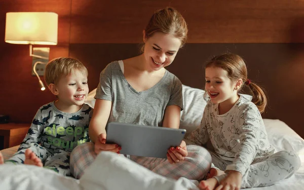 happy family mother and children with tablet computer at home in bed in the evening