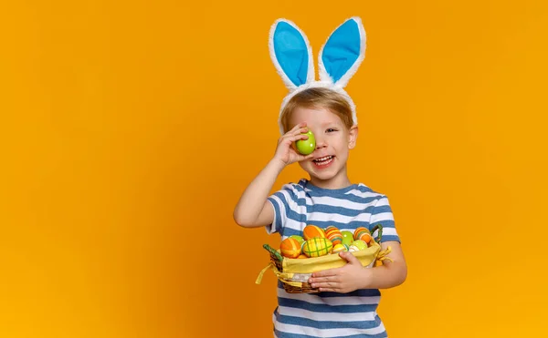 Grappige gelukkig kind jongen met paaseieren en bunny oren op yello — Stockfoto