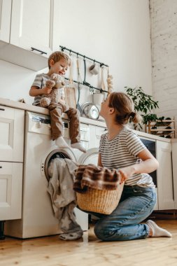 Mutlu aile annesi, ev hanımı ve oğlu çamaşır makinesiyle çamaşır yıkıyor.
