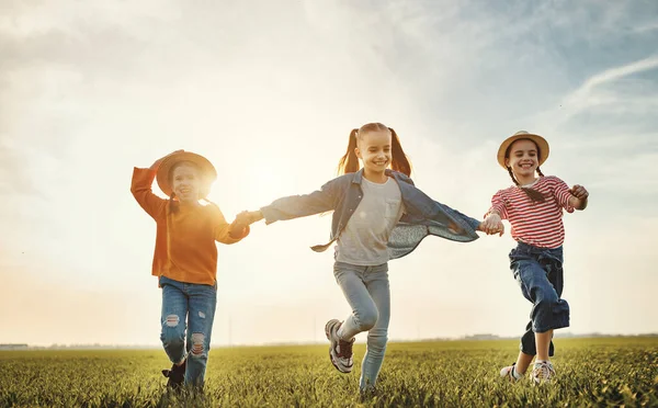 陽気な子供たちは笑顔で緑の芝生の上を走りながら 太陽の下で牧草地を楽しんでいます — ストック写真