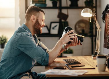 Pozitif genç erkek fotoğrafçının fotoğraf makinesinde resimlere bakıp evde çalışırken güldüğü yan manzara.