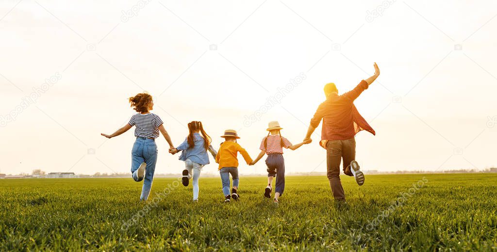 Unrecognizable happy   parents with daughters in casual clothes running back with holding hands while enjoying time together on green meadow in summer evenin