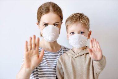 Tıbbi maskeli yetişkin bir kadın ve küçük bir çocuk Coronavirus salgını sırasında gri bir gruba karşı kameraya bakıyor.