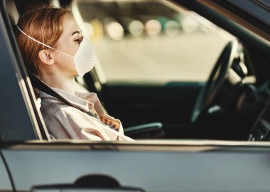 Tıbbi maskeli yetişkin bir kadın Coronavirus Outbrea sırasında modern araba koltuğunda oturuyor.