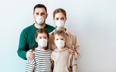 Tıbbi maskeli aileler ve çocuklar bulaşıcı koronavirüs salgını sırasında gri duvara bakarken kameraya bakıyorlar.