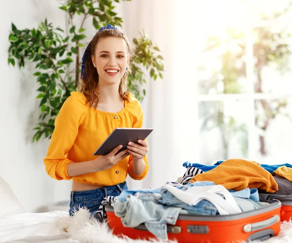 快乐的年轻女人用平板电脑核对物品清单 收拾行李 为旅行 旅行做准备 — 图库照片