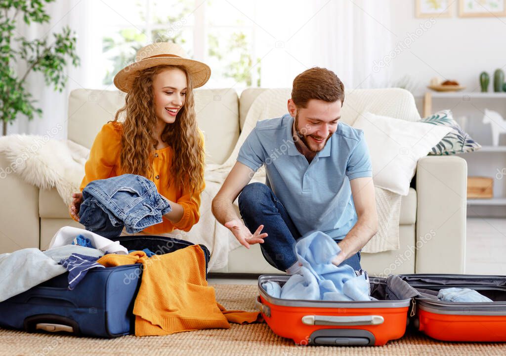 Laughing man and woman in summer hat setting off for journey and packing bags on floor in living room anticipating vacatio