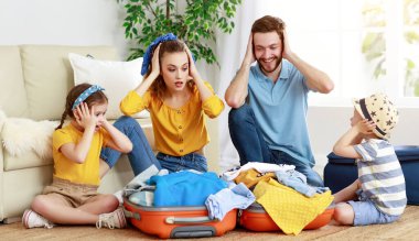 Küçük çocukları bavullarını toplayan neşeli ebeveynler yerde oturup kulaklarını tıkıyorlar.