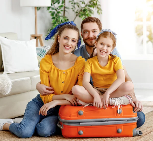 笑着的夫妇和迷人的小女孩坐在客厅的行李箱上 高兴地看着准备放暑假的相机 — 图库照片