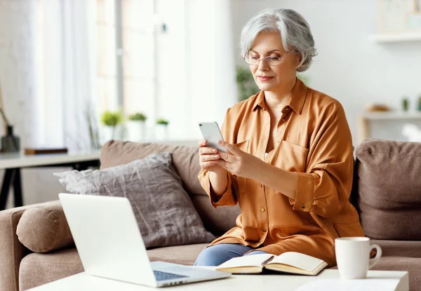 Senior Woman Sitting Couch Table Notepad Laptop Browsing Smartphone While — Stock Photo, Image