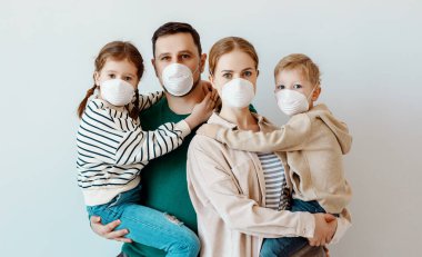 Bulaşıcı koronavirüs epidemi sırasında gri duvara bakarken tıbbi maskeli aileler ve çocuklar kameraya bakıyor.