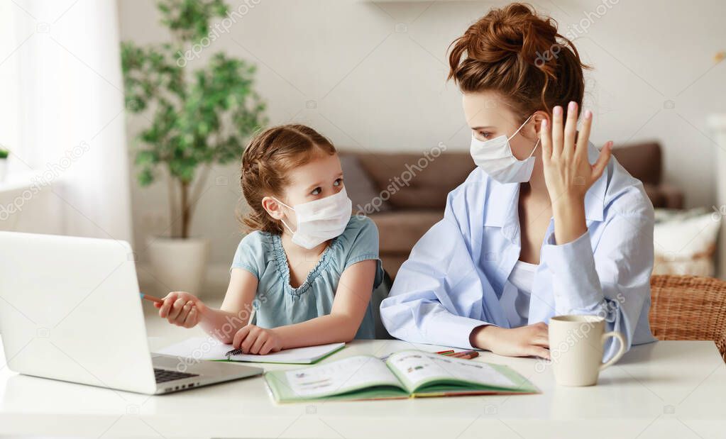 Little girl in medical mask pointing at laptop and looking at irritated mother while sitting at table and doing homework together during quarantin