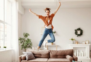Kablosuz kulaklıklar ve günlük kıyafetlerle hafif modern yaşam kangurusunda kanepe zevkle müzik dinleyen ve dans eden neşeli genç bayanın alçak açısı.