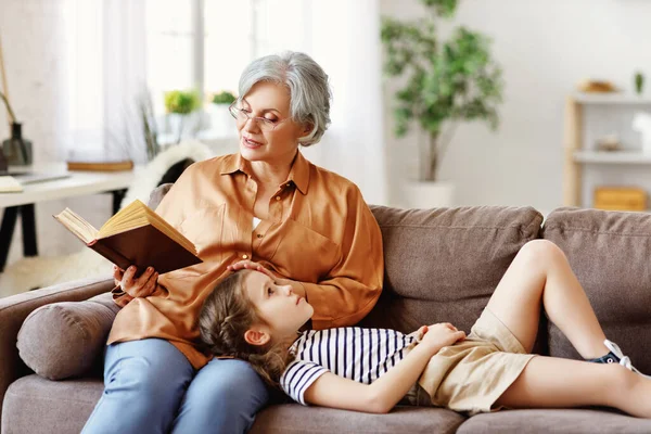 Senior Woman Sitting Couch Reading Fairytale Attentive Little Girl While — Stock Photo, Image