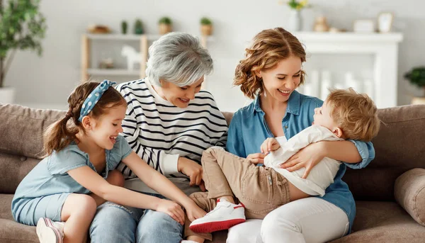 Büyükanne ve anne, hafta sonları evde çocuklarla oynaşırken ve kanepede oturup gülen çocuğu kucaklıyor ve gıdıklıyor.