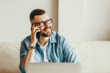 Genç, yakışıklı, serbest çalışan ve evde telefonla konuşan bir adam.