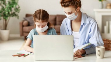 Maskeli bitkin bir kadın, salgın sırasında laptopta çalışırken masada oturup çalışkan bir kızın çalışmasını izliyor.