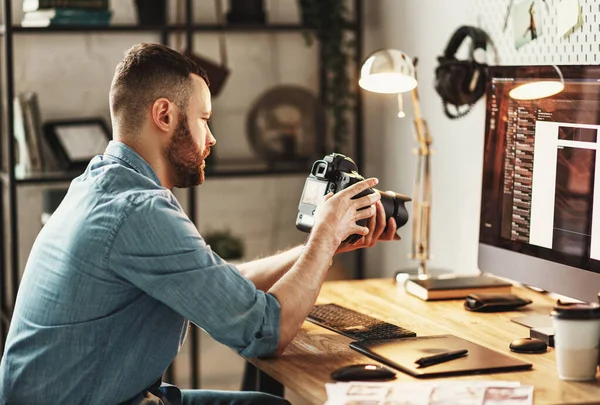 Ciddi bir genç fotoğrafçının fotoğraf makinesinde resimlere bakıp evde çalışırken gülüşünün yan görüntüsü.