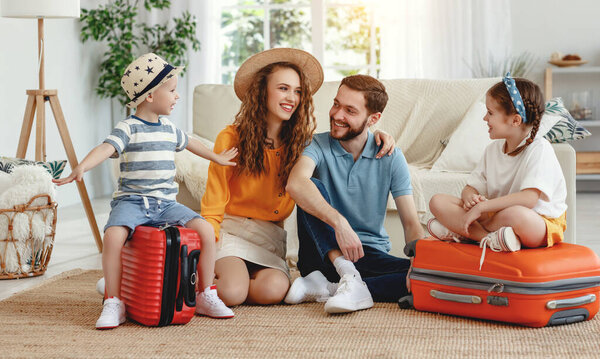 Happy parents with children laughing   while sitting on floor near sofa with suitcases near at hom
