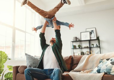 Neşeli baba kanepeye oturup, keyifli küçük çocuğu kusarken modern yaşam kangurusunda eğleniyor ve eğleniyor.