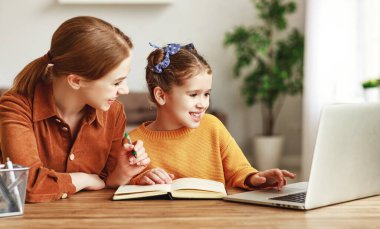 Evde dizüstü bilgisayarla birlikte masada otururken, kızın internette ödev aramasına yardım eden olumlu genç bir kadın.