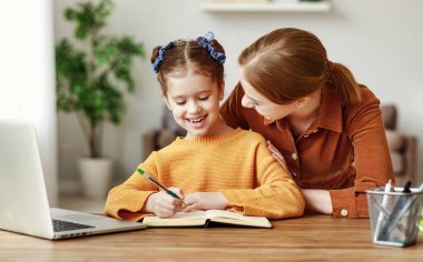 Evde dizüstü bilgisayarla birlikte masada otururken, kızın internette ödev aramasına yardım eden olumlu genç bir kadın.