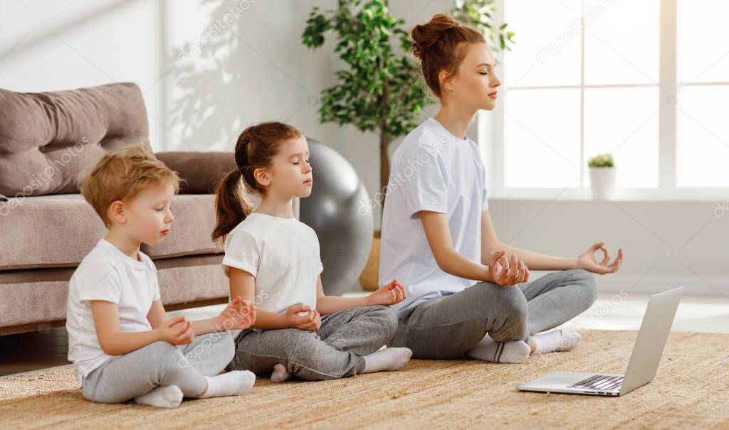 Calm freelance mother with little daughter and song in similar outfits sitting all together in lotus pose and meditating in living roo
