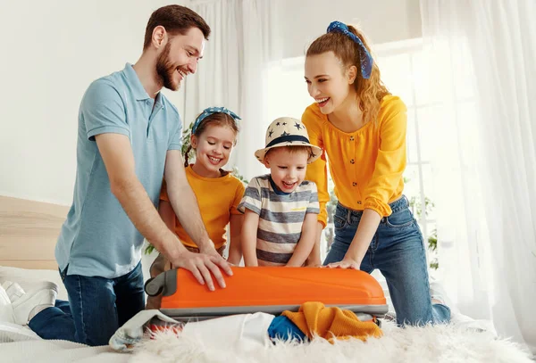 Laughing kids and parents gathering on bed closing suitcase together while getting packed for vacation  with smile