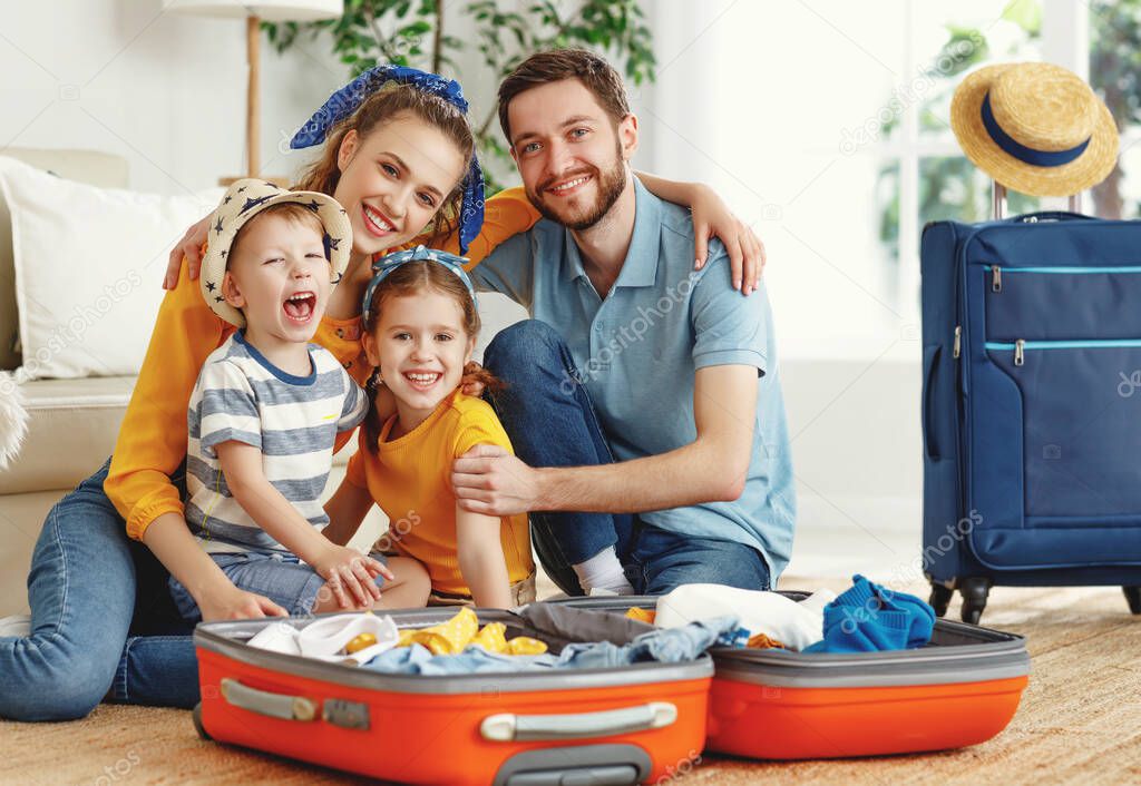Happy parents with children laughing at camera while sitting on floor near sofa with suitcases near at hom