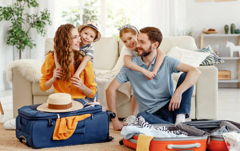 Happy parents with children laughing at camera while sitting on floor near sofa with suitcases near at hom