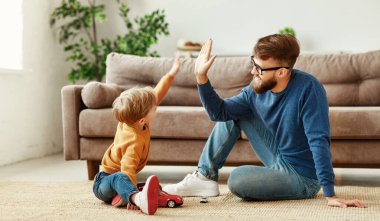 Pozitif sakallı genç bir adam ve küçük bir oğlanın kanepede oturup birlikte eğlenirken beşlik çakışının yan görüntüsü.