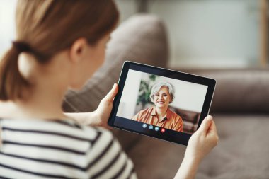Genç bir kadın, dizüstü bilgisayarla yaşlı bir anneyle video sohbetinden zevk alırken kendisi kanepede oturuyor. 