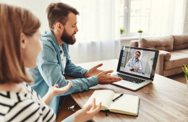 Genç bir adam ve bir kadın, erkek doktor psikologla konuşurken evdeki psikoterapi kliniğine video çağrısı yapıyor.