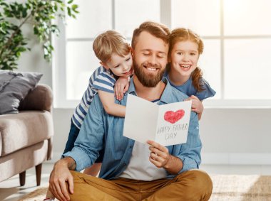 Neşeli küçük çocuk ve kız babalar günü ile mutlu babayı kutluyor ve evde birlikte tatil yaparken el yapımı tebrik kartı veriyor.