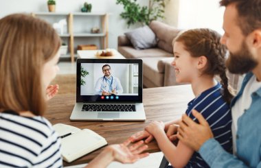 Modern ailelerin yüksek açılı ve neşeli kızı masada oturuyor ve evdeki online doktorla konuşuyor.