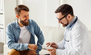 Genç sakallı adam, modern konukseverliğin ofisindeki kanepede otururken dost canlısı erkek doktorla konuşuyor.