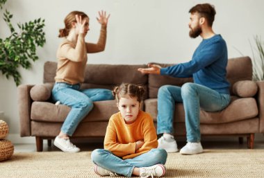 Kızgın ebeveynler kanepede karşılıklı oturuyorlar. Yüksek sesle küfrediyorlar ve elleriyle el kol hareketi yapıyorlar. Bu arada üzgün, savunmasız küçük kız yerde oturmuş kameraya bakıyor.