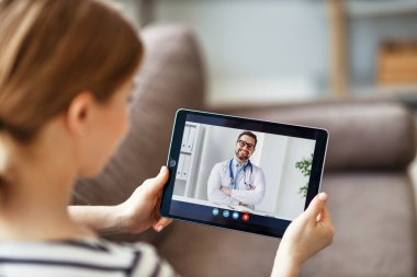 Yukarıdaki modern kadın kanepede oturuyor ve evdeki doktorlara video çağrısı yapıyor.