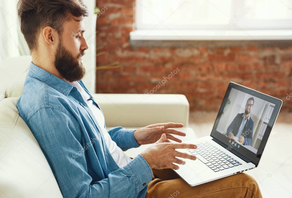 Modern  male sitting on couch and making video call to man financial consultant at hom