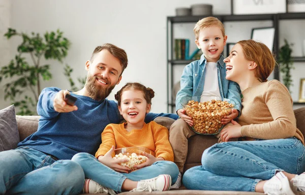 かわいい子供たちと幸せな若い両親は自宅のリビングルームでソファに座って ポップコーンを食べながら面白い映画を見て 週末を一緒に楽しむ — ストック写真