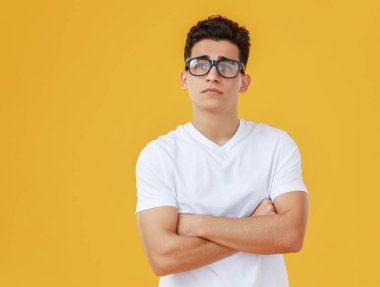 Beyaz tişörtlü, gözlüklü, kollarını kavuşturup sarı arka gruba karşı dik dik bakan zeki etnik erkek.