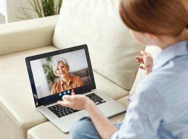 Genç bir kadın, yaşlı bir anneyle kanepede otururken dizüstü bilgisayarla video konuşmaktan zevk alıyor. 