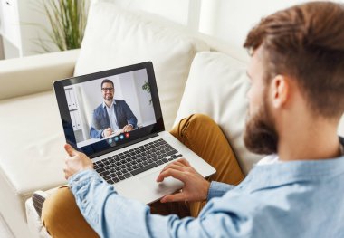 Modern erkek kanepede oturuyor ve evdeki adama video görüşmesi yapıyor.