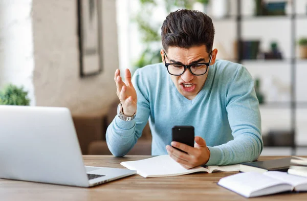 Molesto Joven Étnico Masculino Gafas Gesticulantes Lectura Mensaje Desagradable Teléfono —  Fotos de Stock