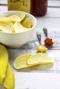 patates cipsi üzerinde beyaz cam kase kaşık ile hardal ve kırmızı biber