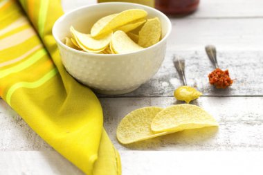 patates cipsi üzerinde beyaz cam kase kaşık ile hardal ve kırmızı biber